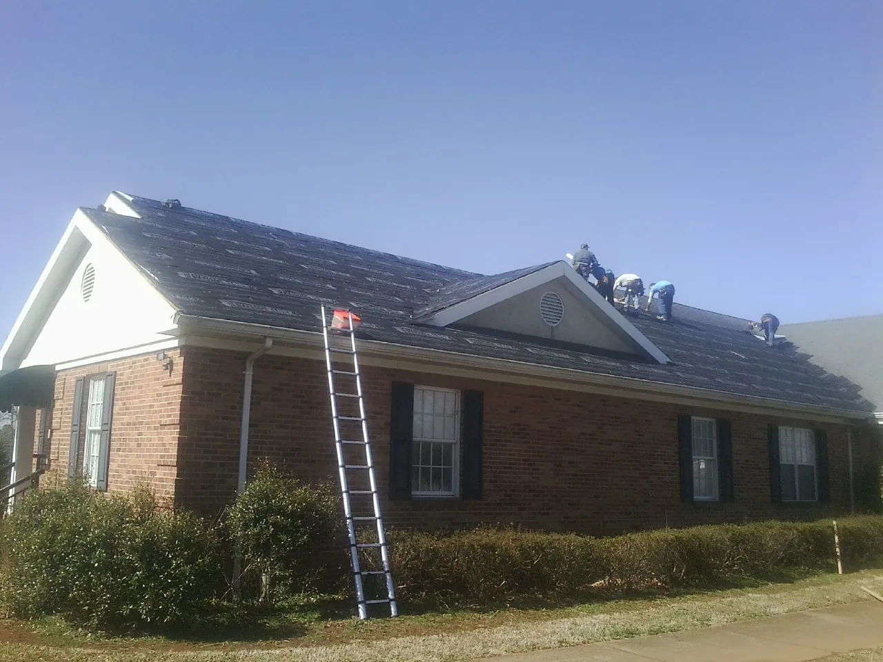 Crew tearing shingles off a brick ranch roof with a ladder set — Metal Roof Repair work by our crew in Patoka