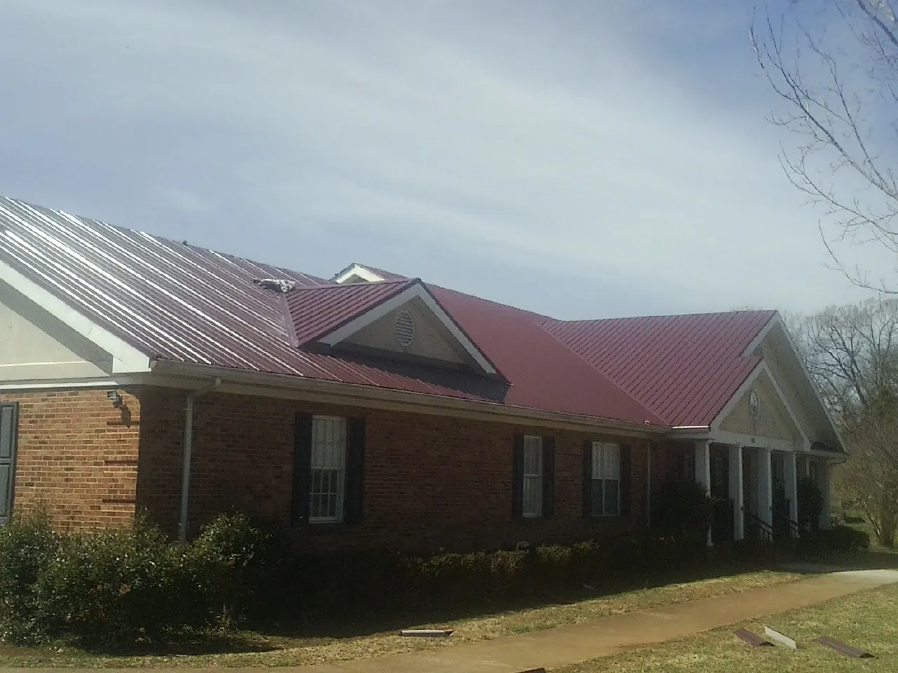 Red metal roof with gabled entries on a long brick building, from a Hail Damage Roof Repair job in Patoka