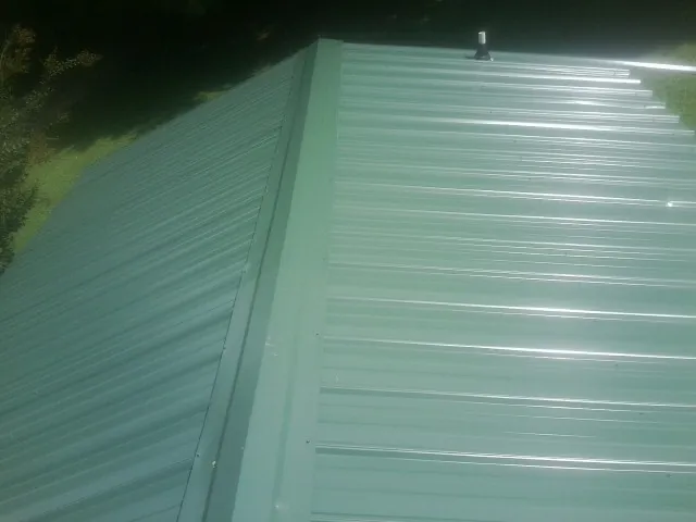 New green metal panels meeting at the ridge of a roof — Flat Roof Repair work by our crew in Patoka