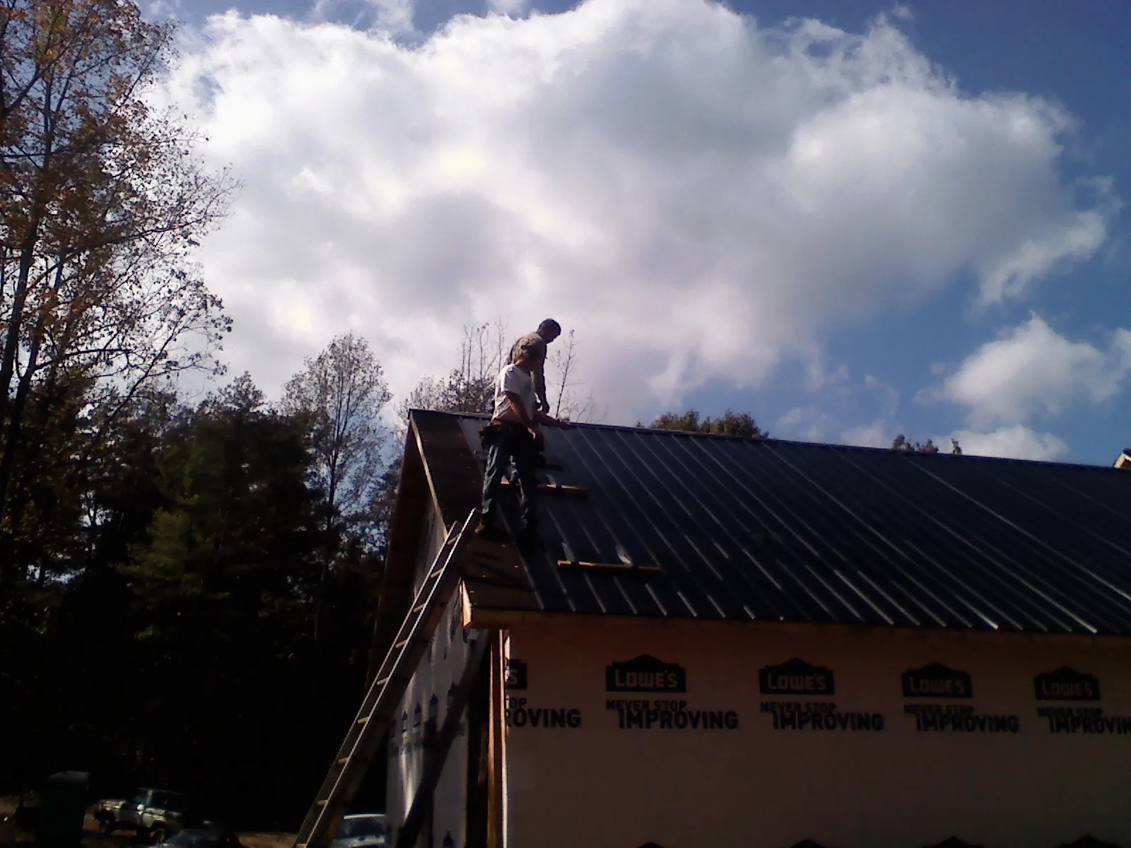 Roofer fastening dark metal panels high against a cloudy sky, from a Roof Inspection job in Patoka