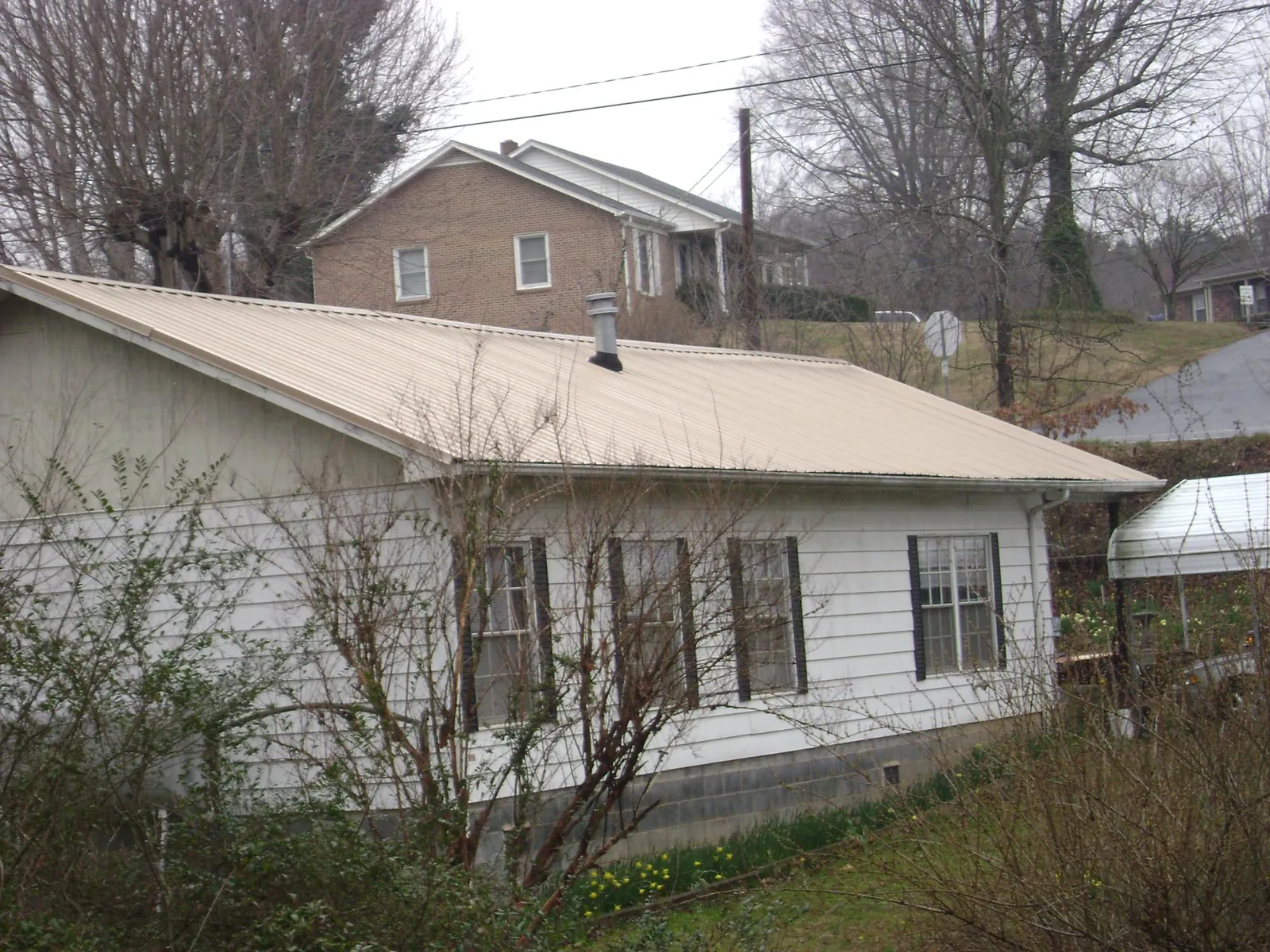 Tan metal roof on a white sided house set into a hillside — Commercial Roofing by Roofing Brothers in Patoka