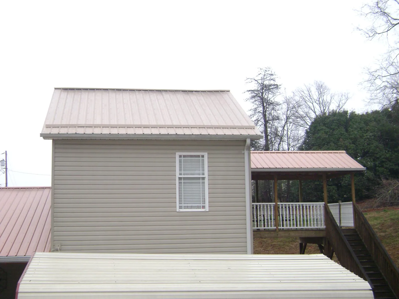Tan metal roofs on a two story addition and attached porch, from a Roof Replacement job in Patoka